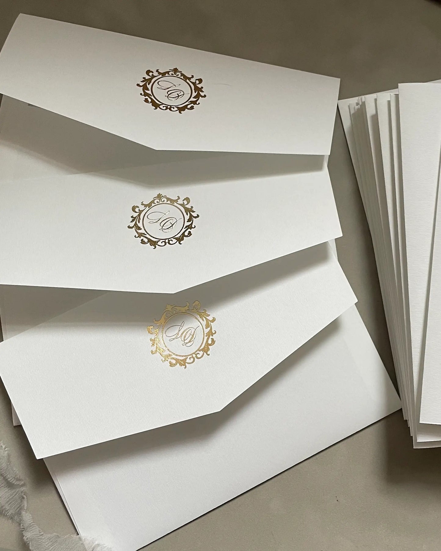 A fan display of premium soft white wedding envelopes for the Buckingham XL suite, featuring custom gold foil stamped monograms on elegant V-shape flaps — Polina Perri