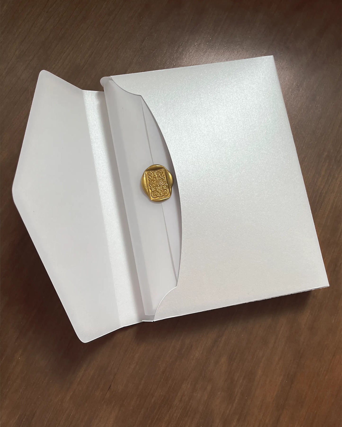 White Velvet Boxed Hampton Manor wedding invitation envelope by Polina Perri, pearlescent white paper envelope sealed with a luxury gold wax stamp on dark wooden background