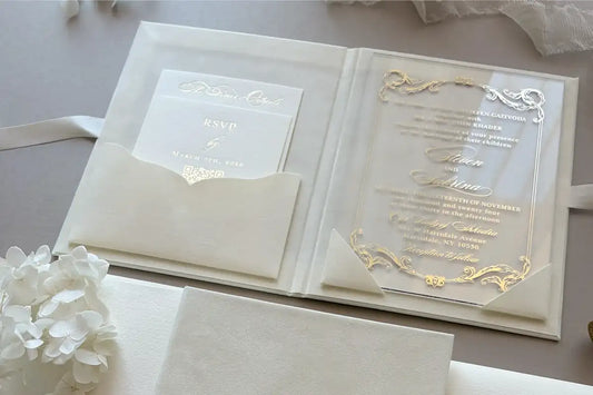 A luxury cream velvet wedding invitation booklet featuring a gold foil embossed monogram crest on the cover, closed with a silk satin ribbon next to a matching envelope with a gold wax seal — Polina Perri