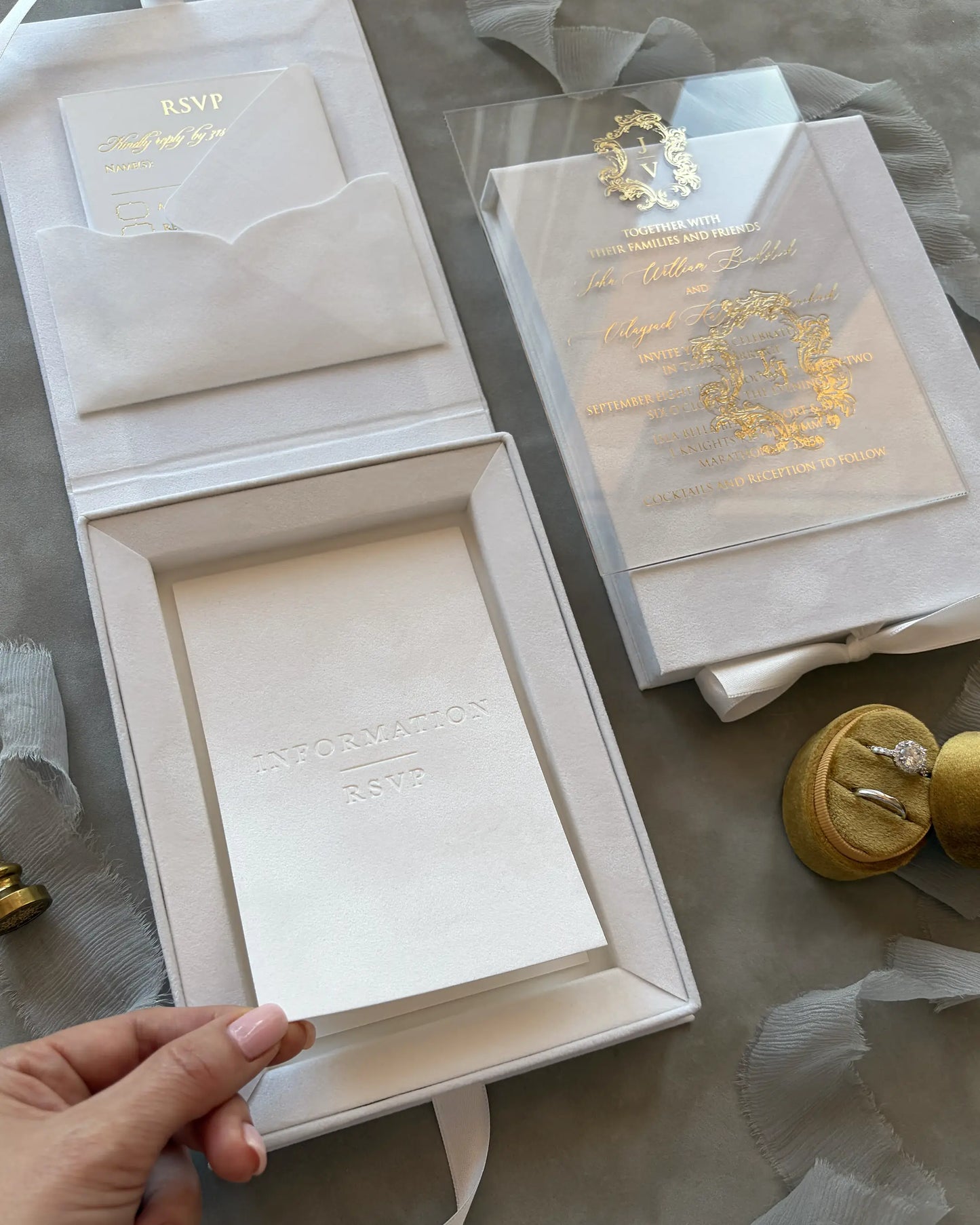 Elegant wedding invitation set with gold emblem on a gray surface. 