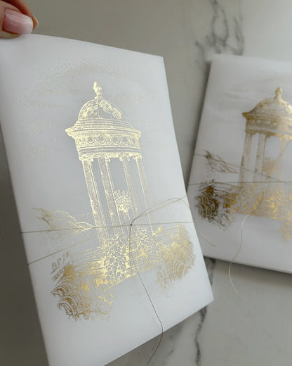 Belvedere luxury destination wedding invitations close up of semi transparent tri fold vellum wrap with gold foil classical pavilion design and delicate gold string Polina Perri