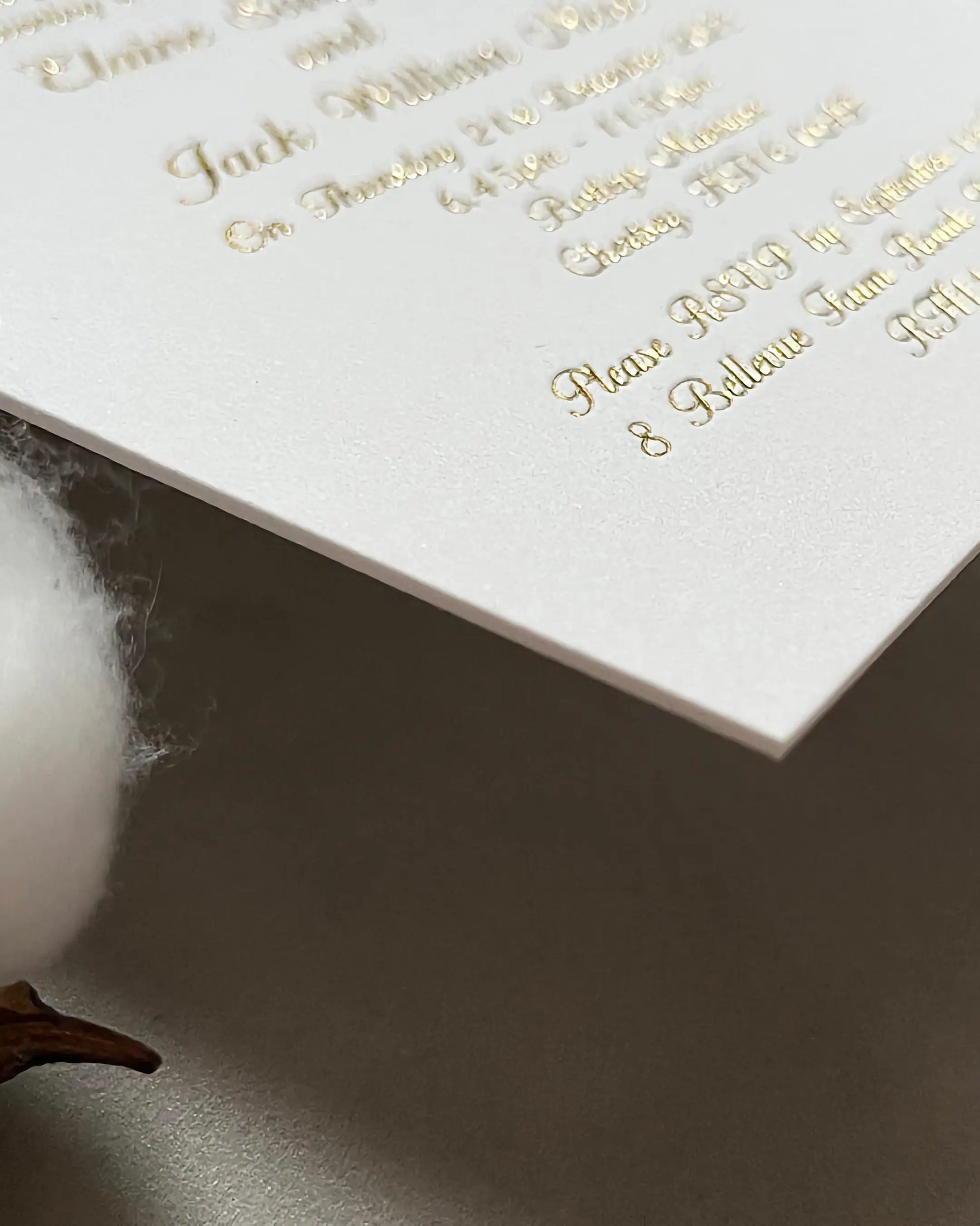Extreme close-up of a venue wedding invitation corner, showcasing the premium tactile texture and thickness of the 600gsm cotton paper stock with crisp gold foil text — Polina Perri