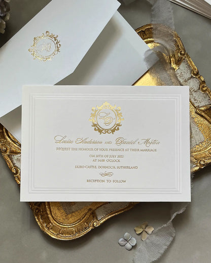 Buckingham XL luxury wedding invitation on soft white 600gsm cotton card stock, featuring a blind embossed 3D border and gold foil typography, presented with a matching monogrammed envelope on a vintage gold tray — Polina Perri