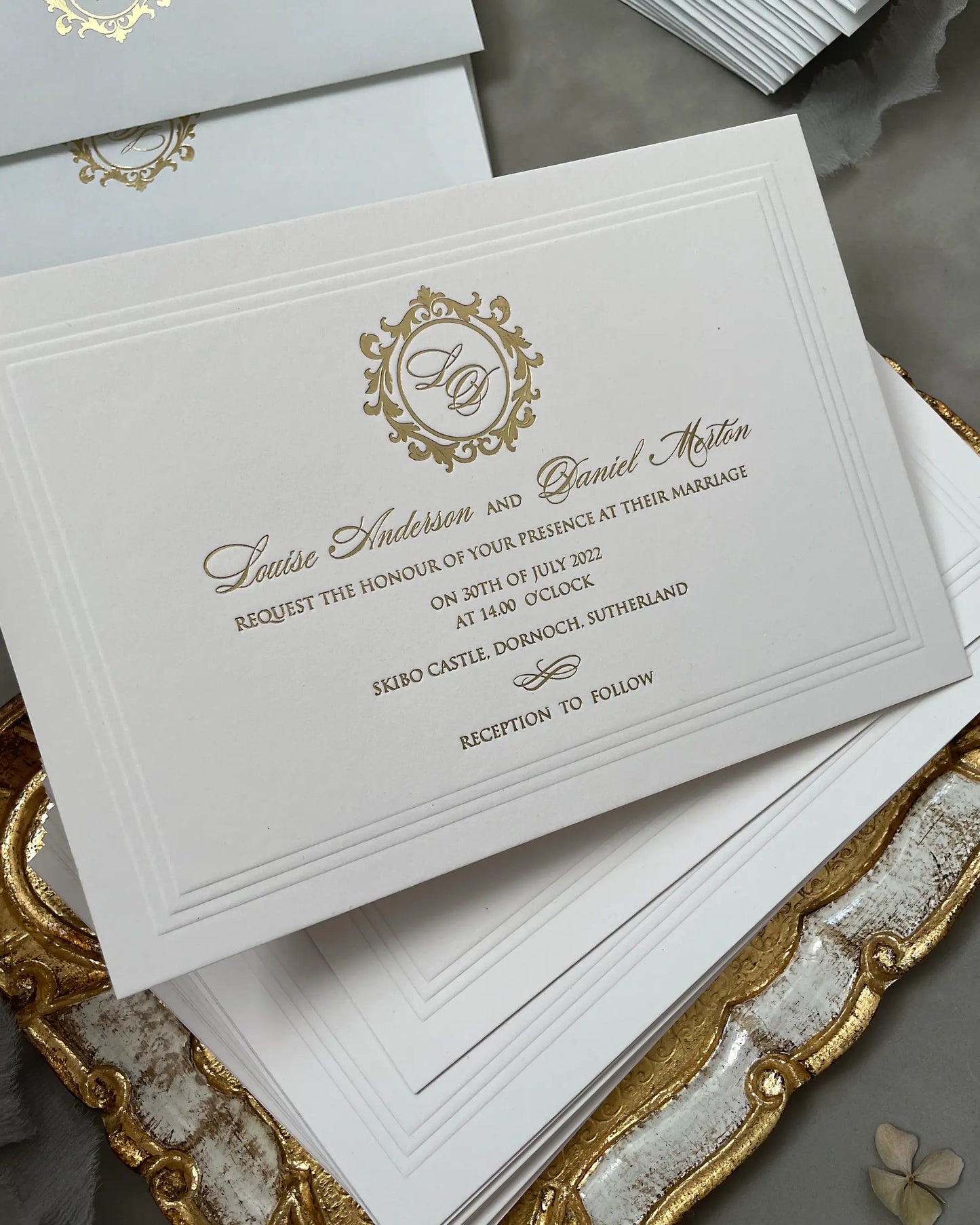Angled close-up of a stack of Buckingham XL wedding invitations, showcasing the heavy texture of 600gsm cotton paper and the detailed gold foil stamped crest with a blind debossed frame — Polina Perri