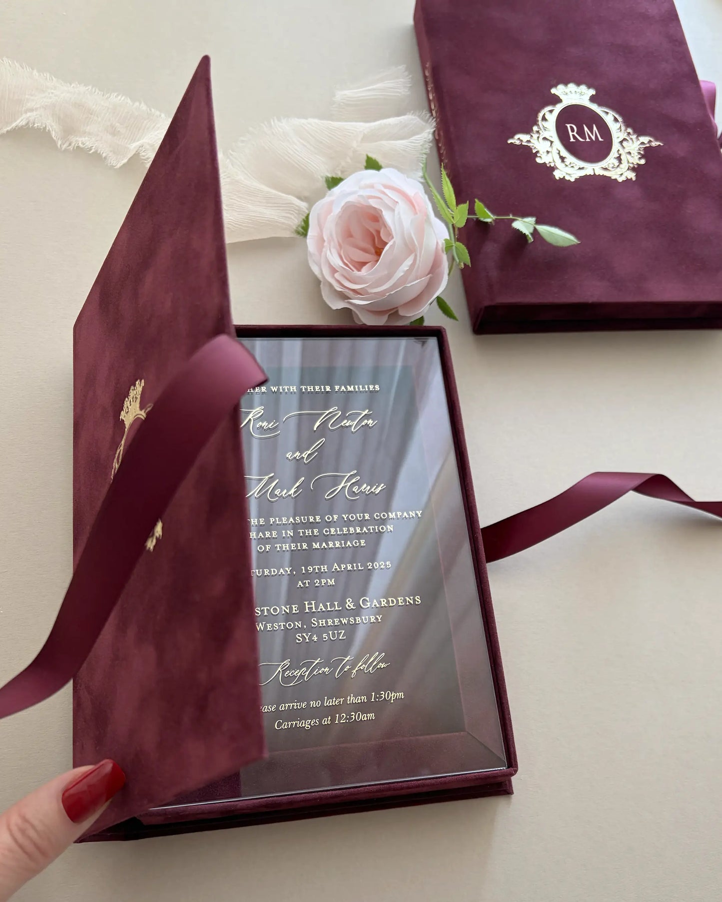 Elegant burgundy velvet book-style wedding invitation box being opened to reveal a premium frosted acrylic invitation card with hot foil pressed typography — Polina Perri