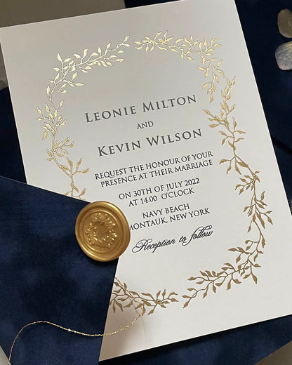 Close-up of the Celeste wedding invitation with a gleaming gold foil pressed botanical wreath on white cotton paper, accented by a navy blue envelope and gold wax seal — Polina Perri