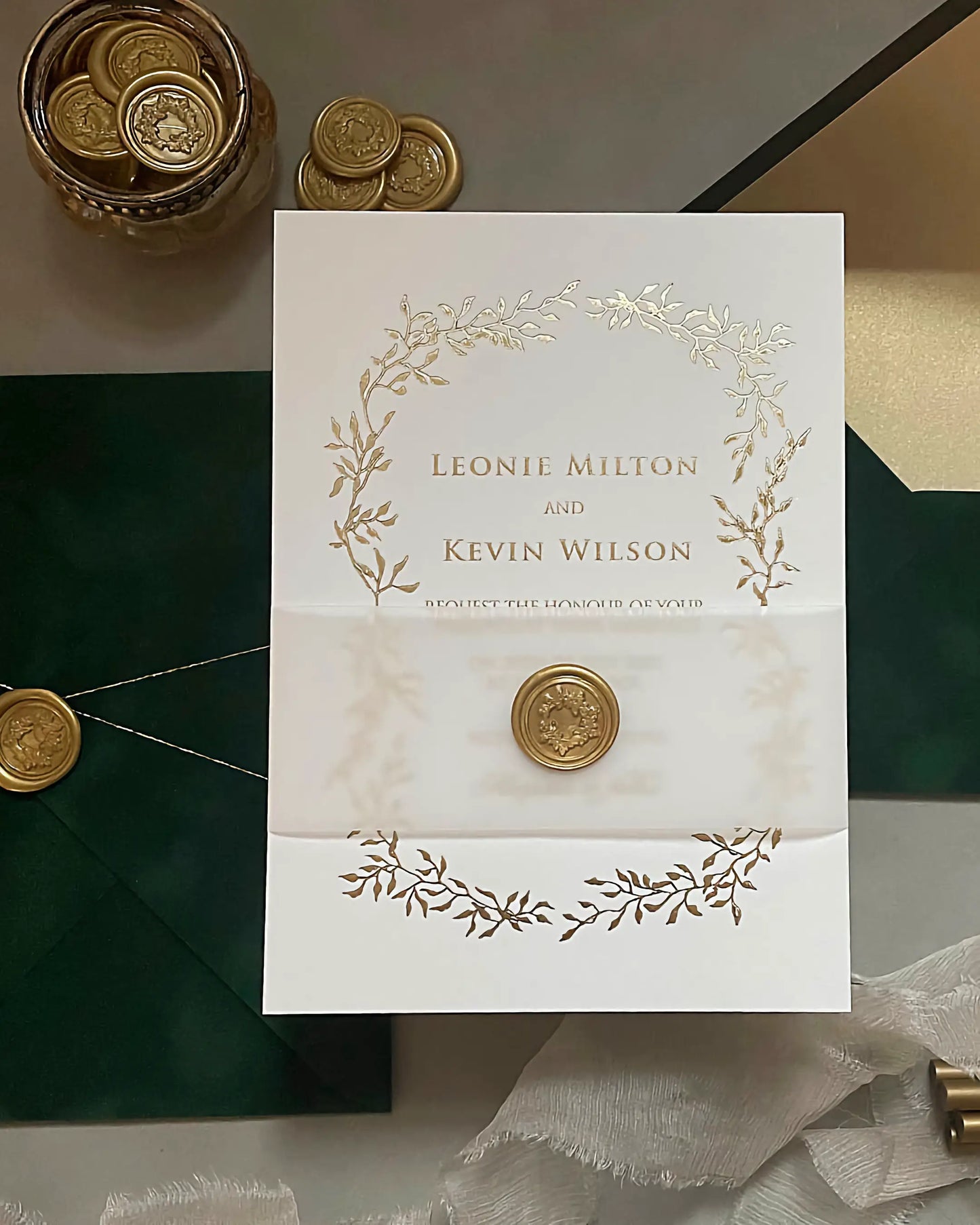 Elegant wedding invitation with gold foil leaf detailing, secured with a translucent vellum belly band and a personalized metallic wax seal — Polina Perri
