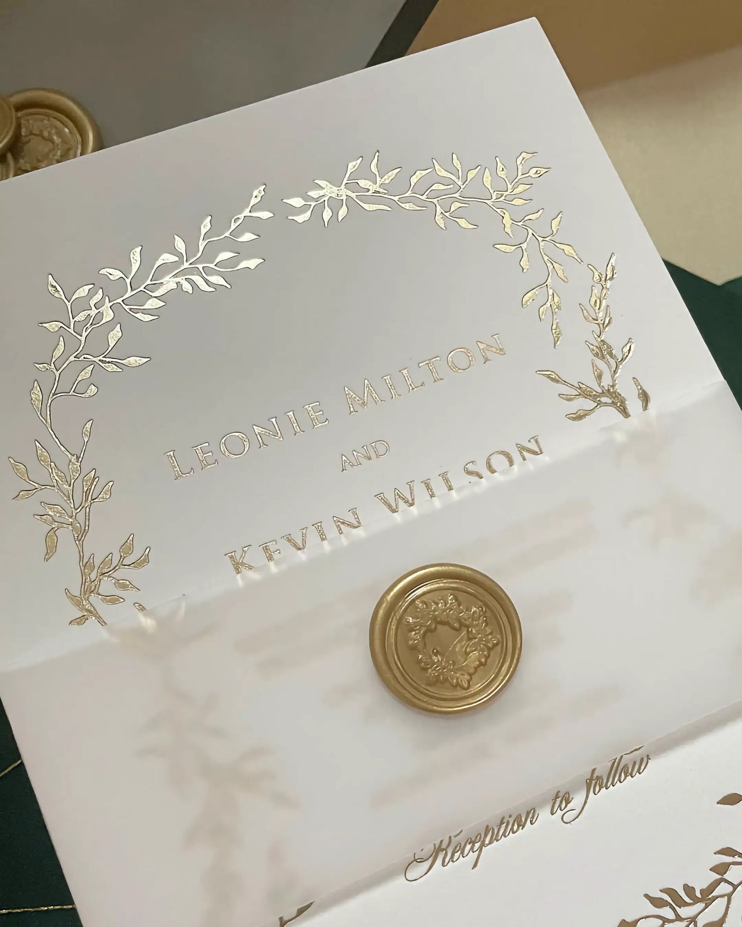 Macro shot highlighting the crisp typography and shimmering gold foil pressed foliage design on a premium white wedding invitation with a vellum band — Polina Perri