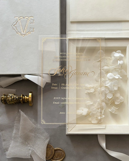Close-up of a luxury clear acrylic wedding invitation with elegant gold foil pressed calligraphy, placed over a premium cream velvet presentation box — Polina Perri