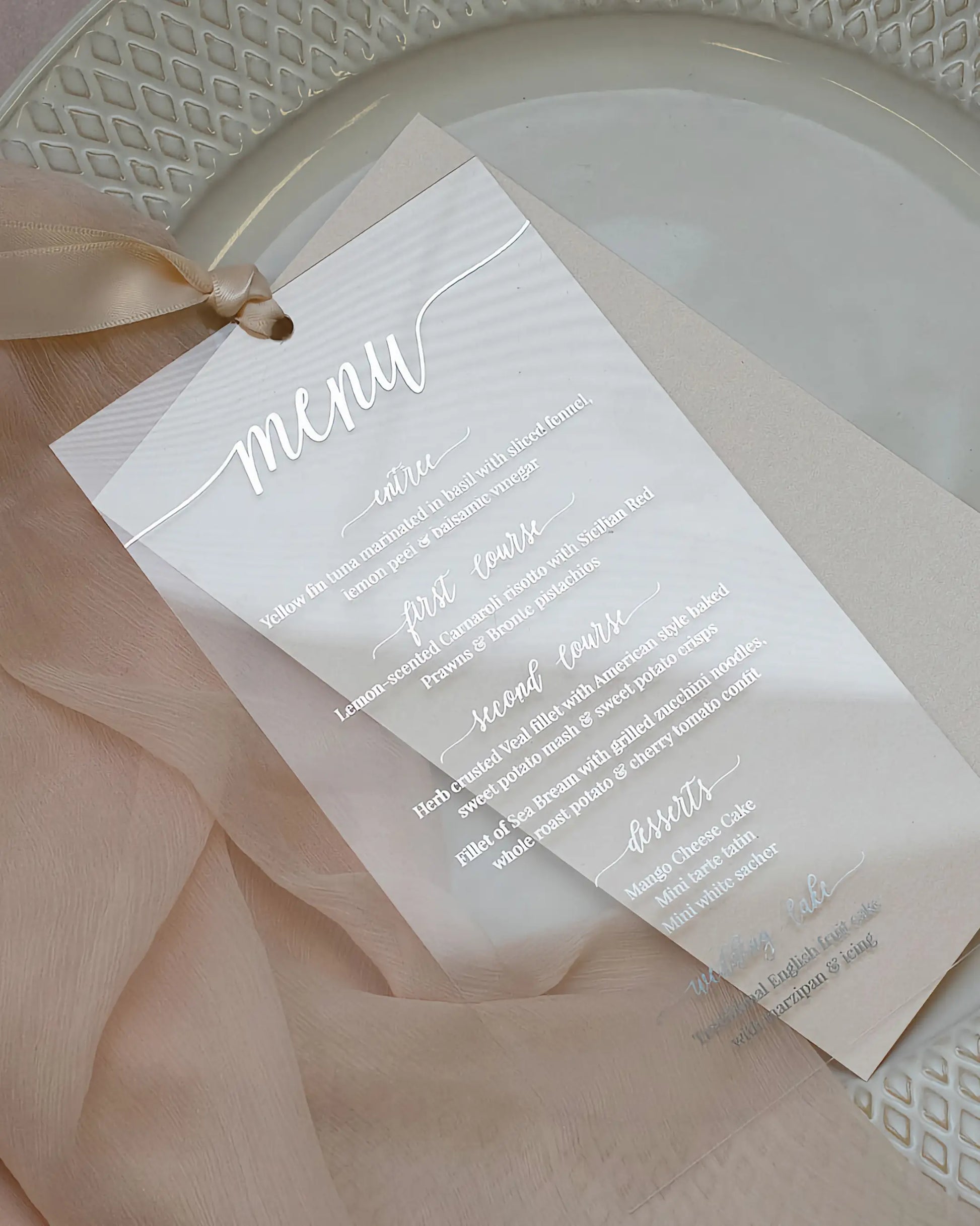 Contemporary wedding table setting featuring a clear acrylic menu card with striking silver foil script positioned on a white textured charger plate — Polina Perri