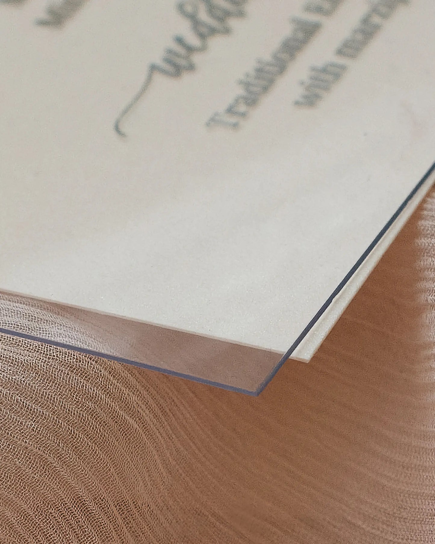 Macro shot showing the clean cut edge and premium 0.5mm thickness of a transparent acrylic wedding menu card layered over textured paper — Polina Perri