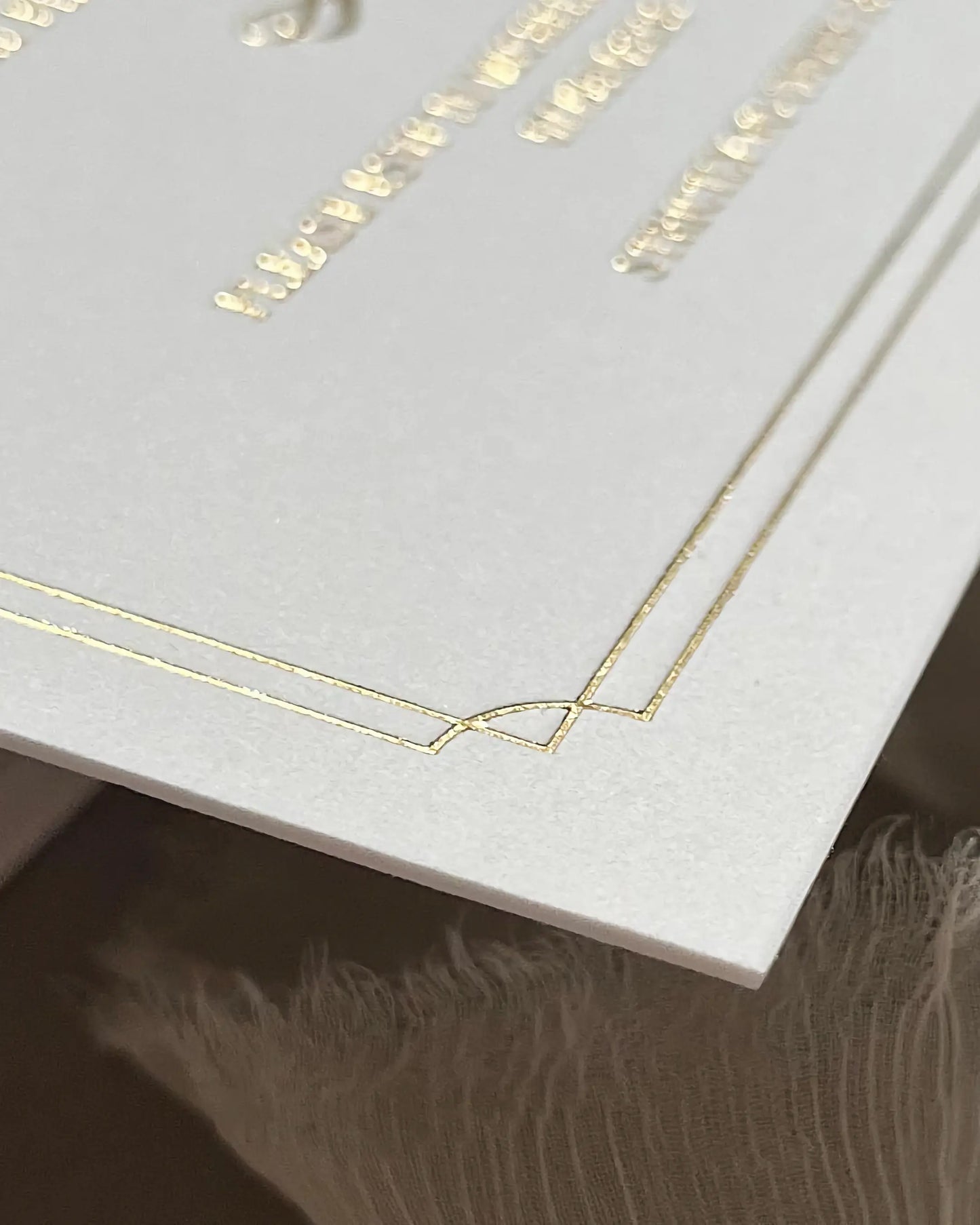 Macro shot displaying the tactile texture of 600gsm white cotton paper and the reflective finish of a double gold foil pressed geometric border — Polina Perri