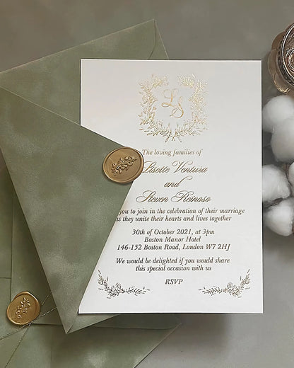 Fiori Gold foil pressed wedding invitation with a botanical floral monogram wreath on luxury white cotton paper, tucked into a sage green envelope with a gold wax seal — Polina Perri
