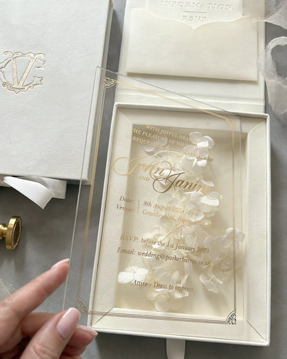 Perspective view of a clear acrylic wedding invitation card with gold foil borders, held to showcase the dimensional white hydrangea flowers inside the velvet box — Polina Perri