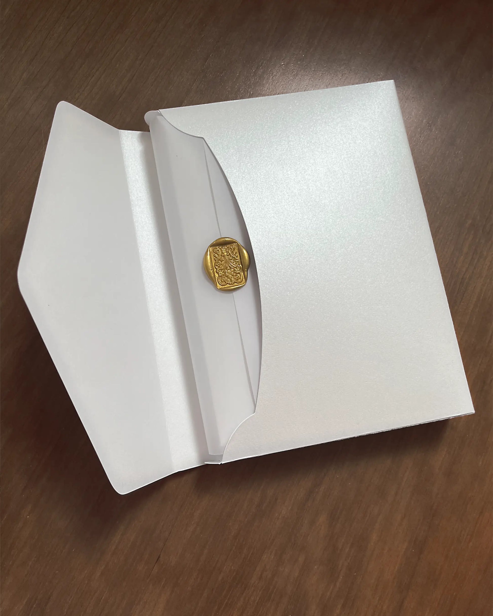 White Velvet Boxed Hampton Manor wedding invitation envelope by Polina Perri, pearlescent white paper envelope sealed with a luxury gold wax stamp on dark wooden background