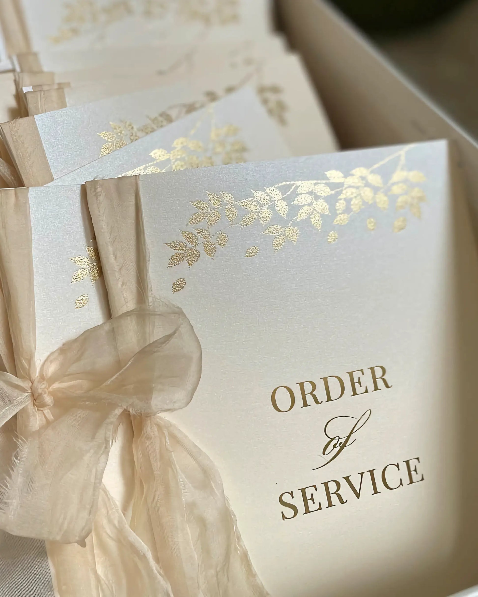 Close-up of a premium wedding ceremony booklet cover showing the elegant Foliage design pressed in shiny gold hot foil on textured ivory cardstock — Polina Perri