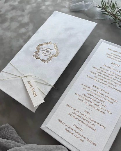 Perspective view of a prestigious white velvet wedding breakfast menu package highlighting the crisp gold stamping and elegant thin cord wrapping — Polina Perri