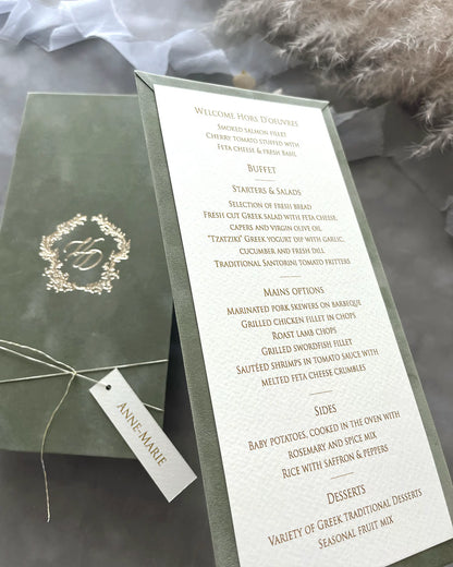 Angled shot of a sage green velvet wedding dinner menu showcasing the premium textured paper card with elegant gold typography and a personalized tag — Polina Perri