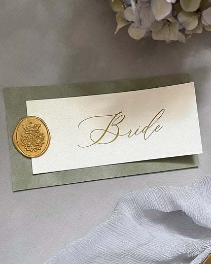 A luxury wedding place card for the bride featuring a sage green French velvet base, transparent vellum overlay with gold foil calligraphy, and a gold wax seal — Polina Perri