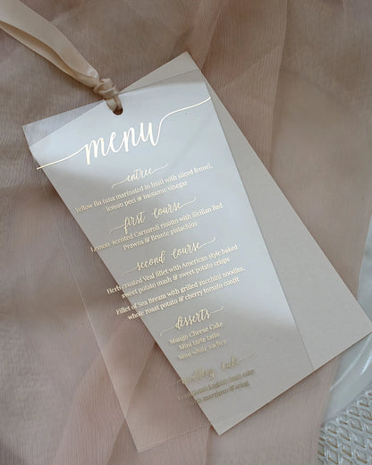 Full view of a transparent wedding dinner menu crafted from high-quality acrylic sheeting with elegant gold foil pressed lettering and a champagne ribbon — Polina Perri