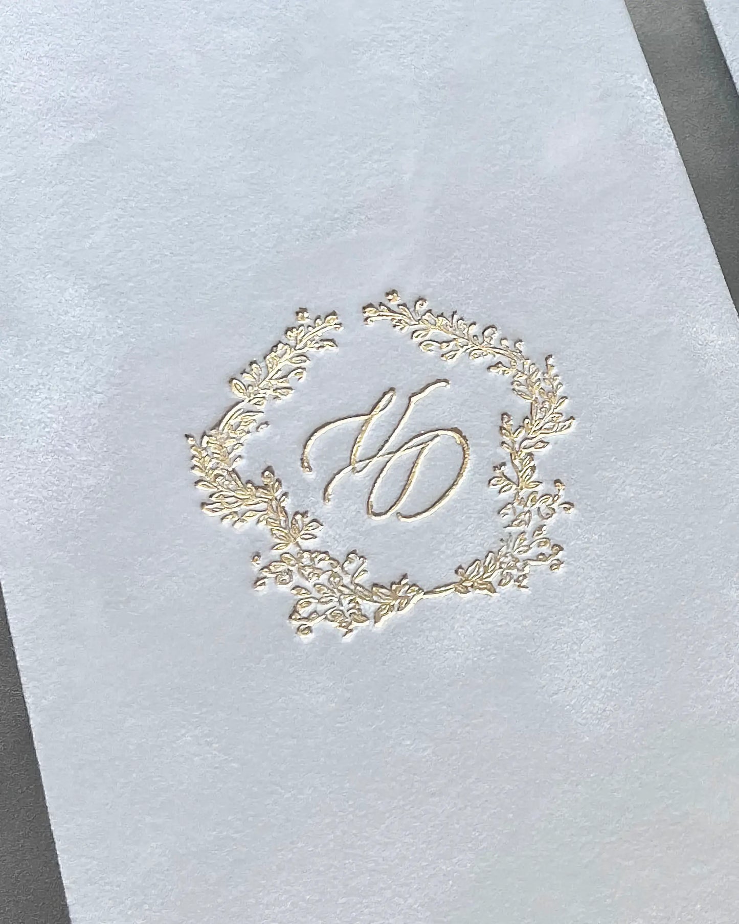 Extreme close-up macro shot revealing the detailed texture of white velvet fabric deeply embossed with a luxury gold foil wedding monogram — Polina Perri