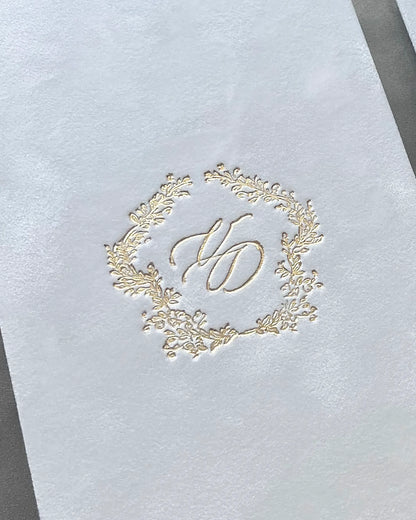 Extreme close-up macro shot revealing the detailed texture of white velvet fabric deeply embossed with a luxury gold foil wedding monogram — Polina Perri