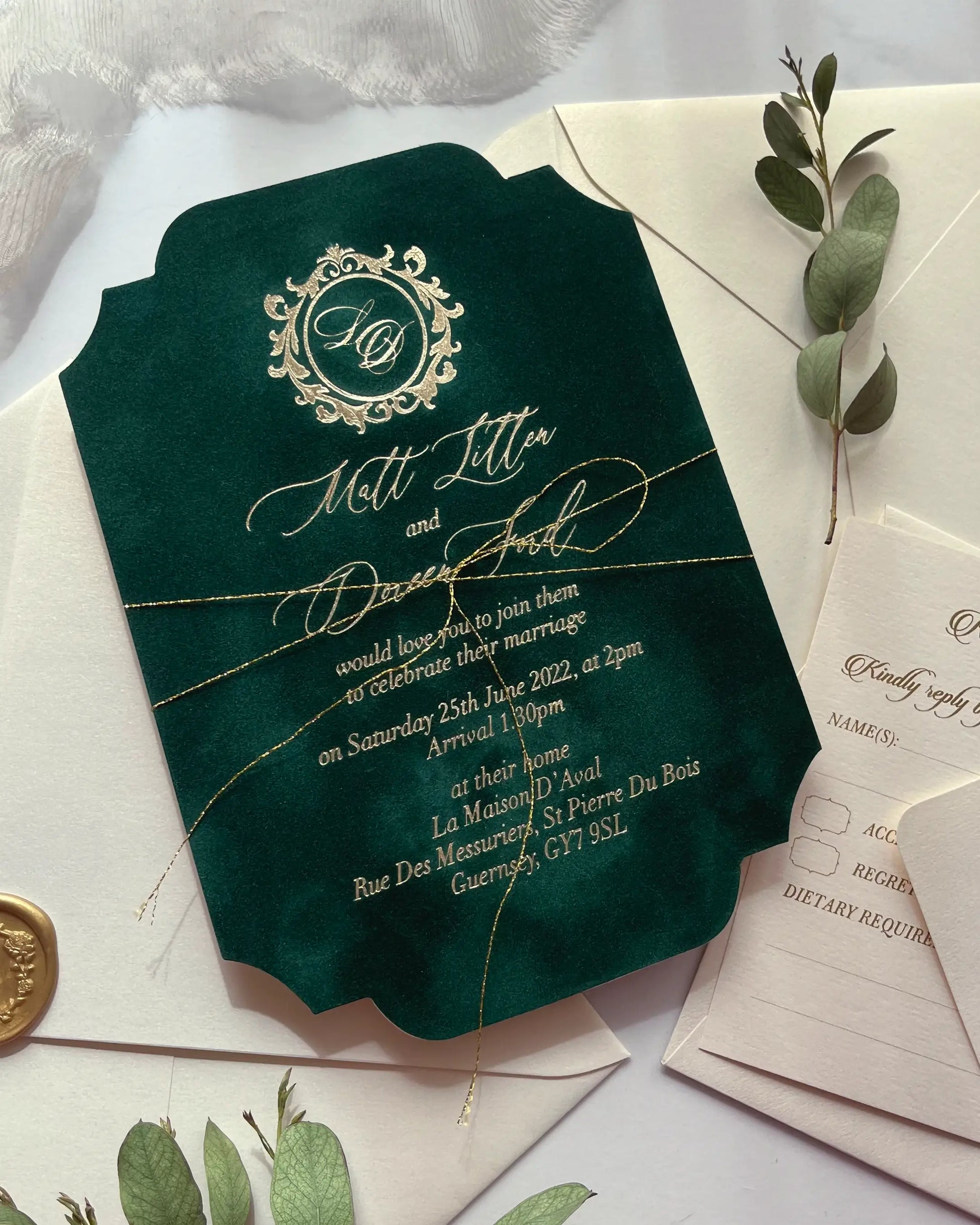 Angled flatlay of a forest green velvet wedding invitation with gold cord styling, textured reply card, and a fresh green eucalyptus branch — Polina Perri