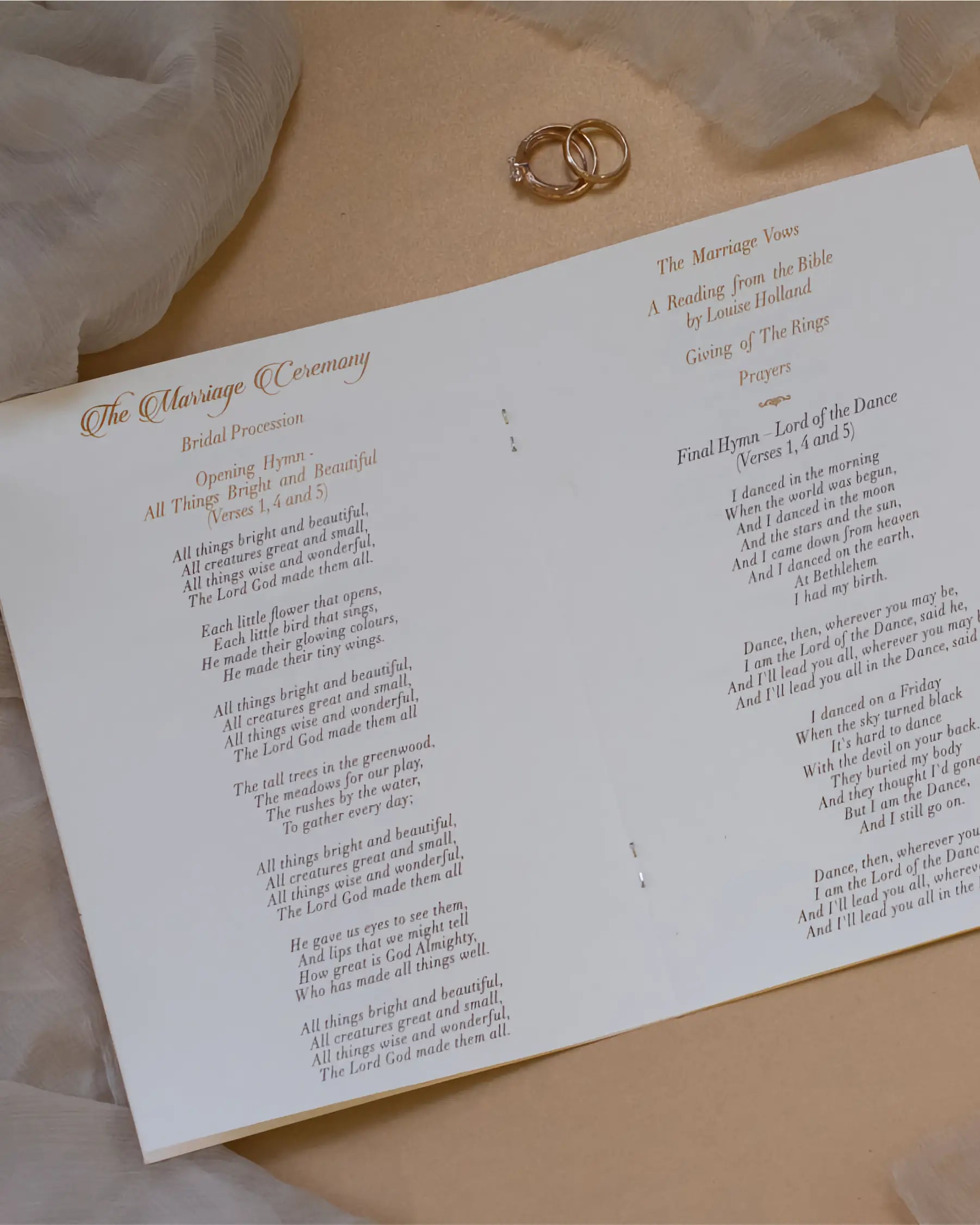 The inner layout of a wedding ceremony booklet showing printed hymns, order of events, and reflective gold foil headings next to a pair of wedding rings — Polina Perri