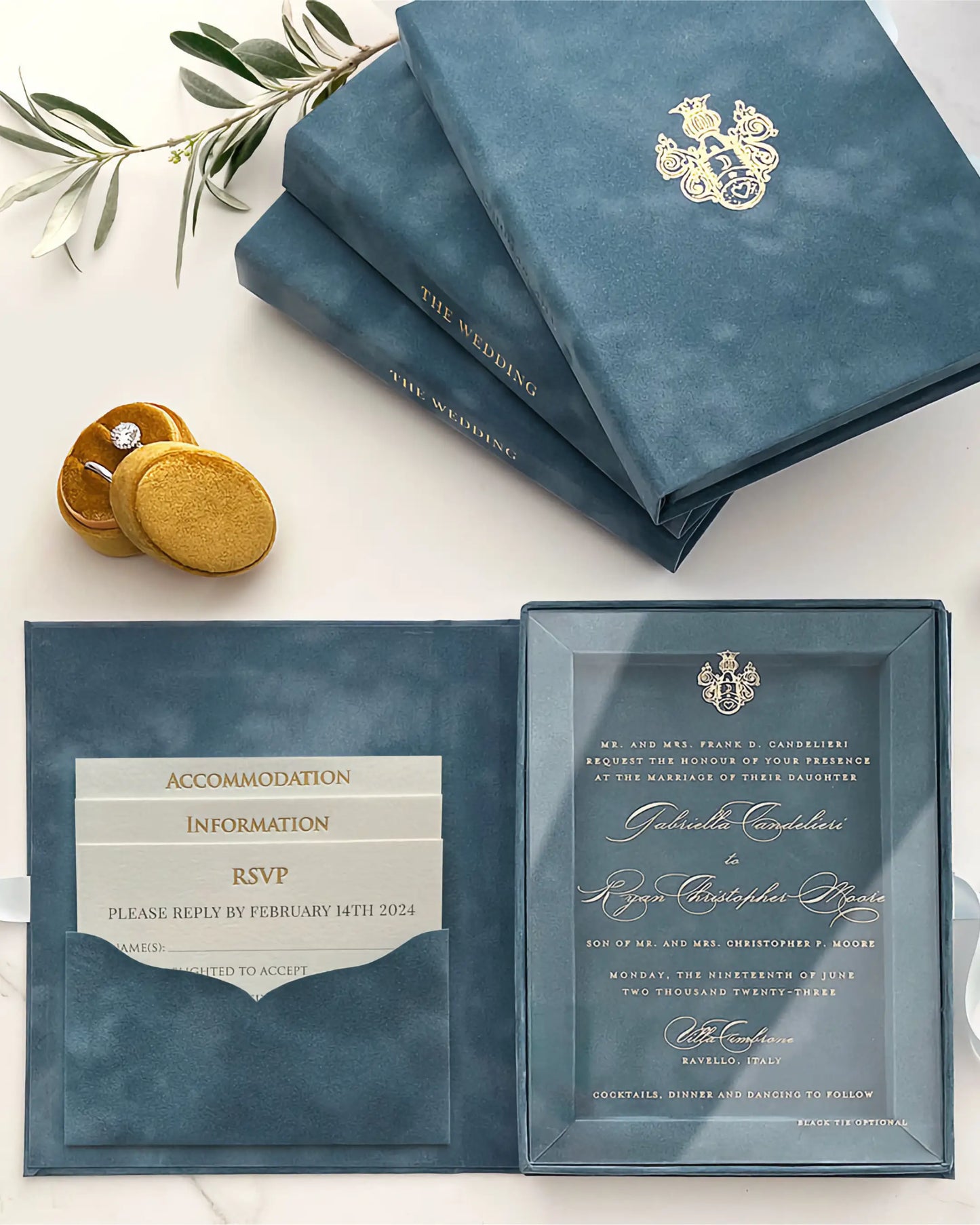 A dusty blue velvet wedding invitation box opened to display a clear acrylic invitation card alongside a built-in pocket holding elegant ivory insert cards for Accommodation, Information, and RSVP — Polina Perri