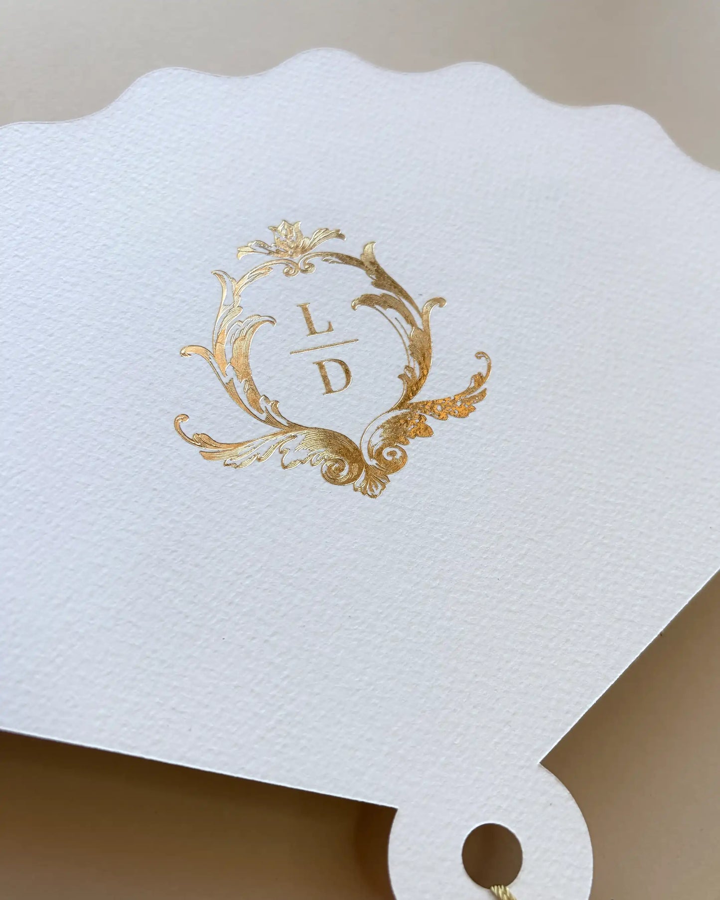A detailed close-up of a white textured fan wedding order of the day, showcasing the ornate gold foil stamped monogram.