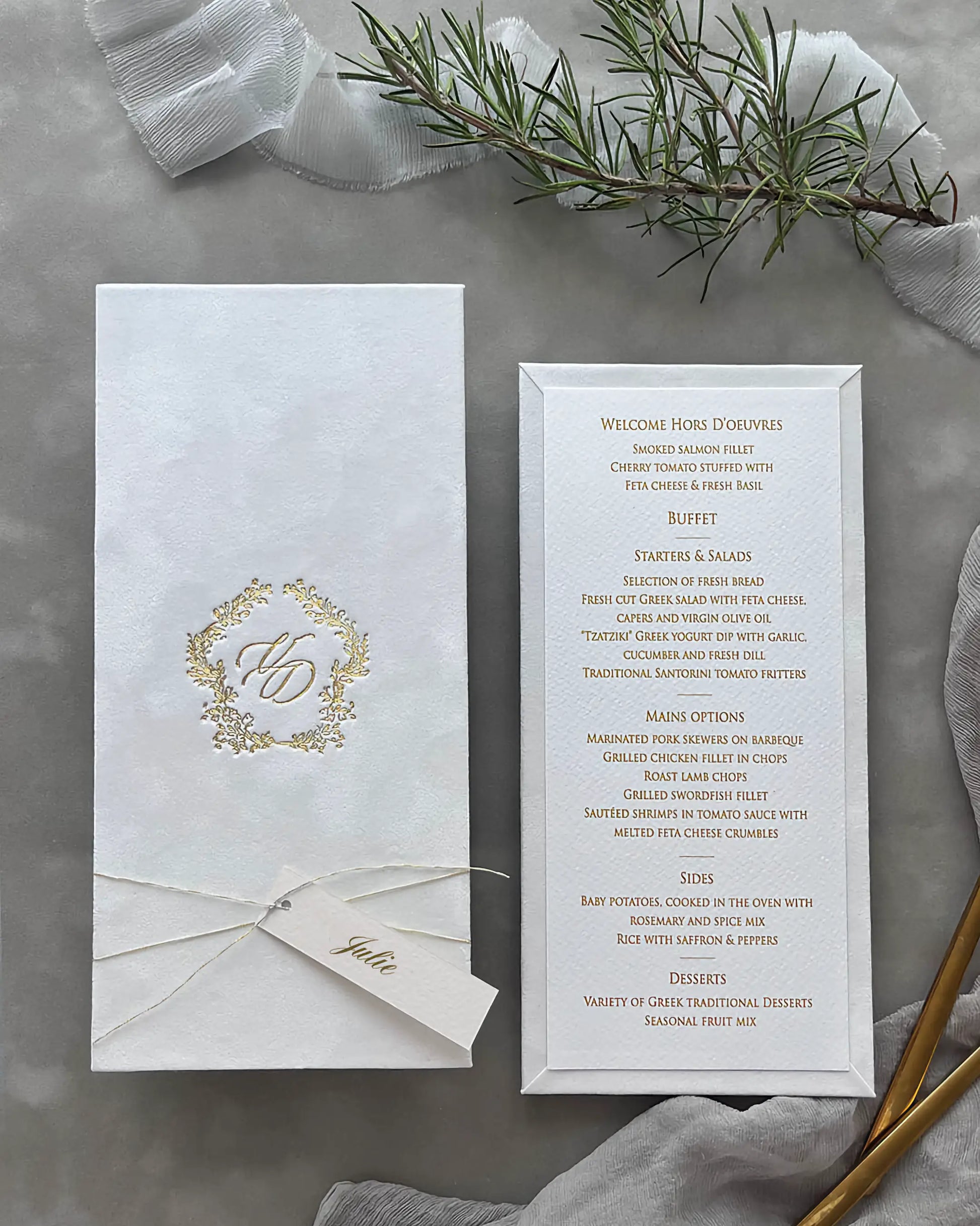 Minimalist white velvet wedding menu card ensemble with a gleaming gold hot stamped emblem cover, ivory cardstock insert, and fresh greenery accents — Polina Perri