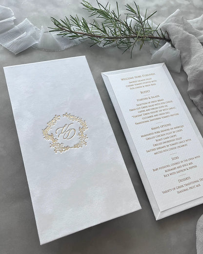 Side angle of a luxury white velvet wedding reception menu booklet presenting custom script font printing alongside a gold foil embossed crest — Polina Perri